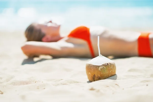 Крупный план на кокосовом орехе и молодой женщины, лежащей на пляже в фоновом режиме — стоковое фото