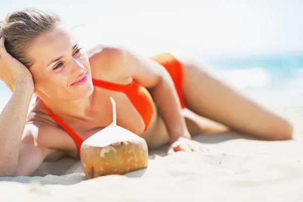 Relaxed young woman laying on beach with coconut — Stock Photo, Image