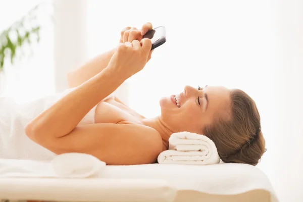 Happy young woman writing sms while laying on massage table — Stock Photo, Image