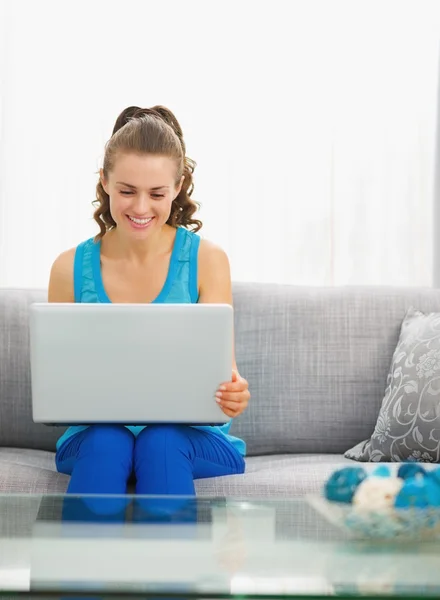 Jovem feliz sentada na sala de estar e usando laptop — Fotografia de Stock