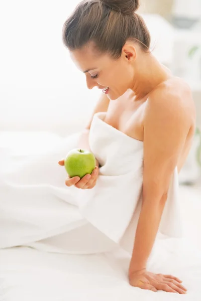Gelukkig jonge vrouw met apple zittend op massagetafel — Stockfoto