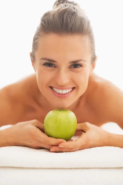 Retrato de mujer joven en mesa de masaje mostrando manzana —  Fotos de Stock