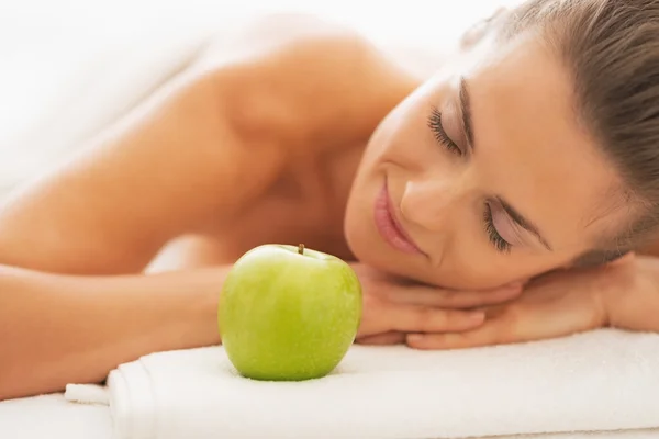 Portrait of relaxed young woman on massage table with apple — Stock Photo, Image