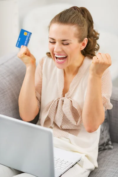 Heureuse jeune femme au foyer avec carte de crédit et ordinateur portable se réjouissant — Photo