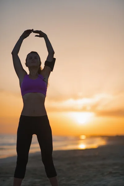 Silueta fitness mladá žena na pláži táhnoucí se za soumraku — Stock fotografie