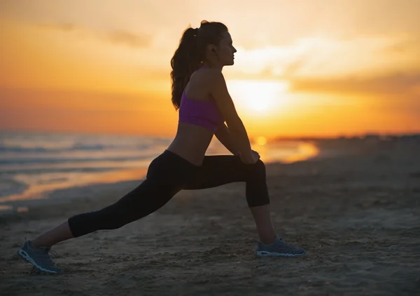 Силуэт фитнеса молодой женщины, растянувшейся на пляже в сумерках — стоковое фото