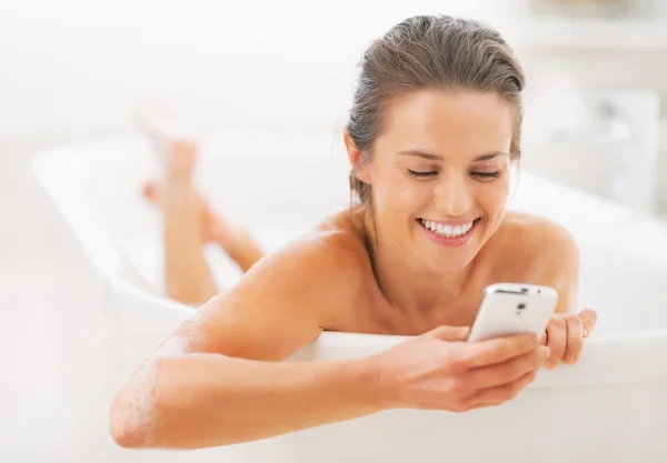 Szczęśliwa młoda kobieta, pisania SMS-ów w wannie — Zdjęcie stockowe
