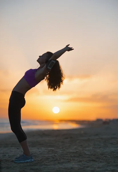 Силуэт фитнеса молодой женщины, растянувшейся на пляже в сумерках — стоковое фото