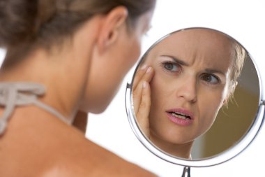 Concerned young woman looking in mirror clipart