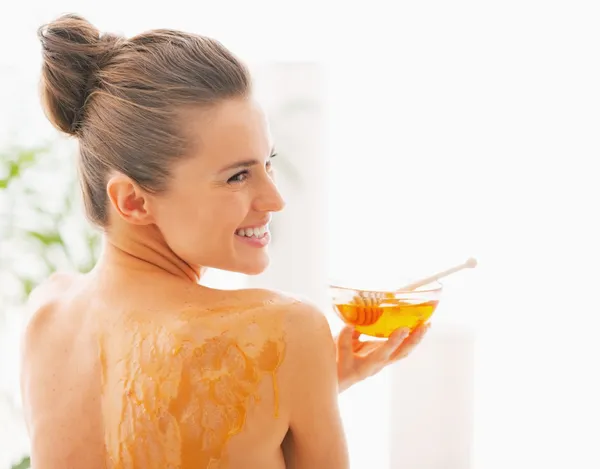Lachende jonge vrouw met honing plaat zittend op massagetafel — Stockfoto