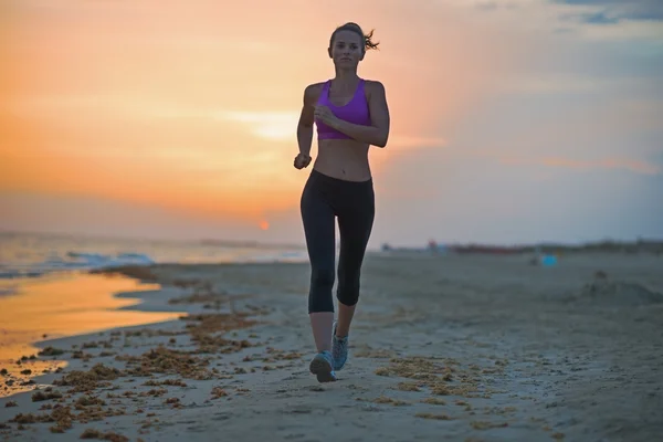 Mujer joven y saludable corriendo en la playa por la noche —  Fotos de Stock