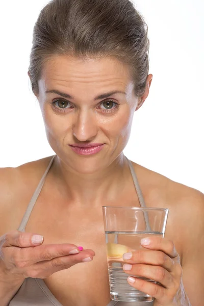 Dudando mujer joven con píldora y vaso de agua — Foto de Stock