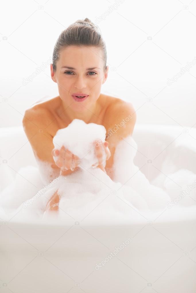 Smiling young woman playing with foam in bathtub