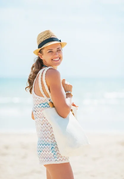 Sorrindo jovem mulher de chapéu e com saco na praia — Fotografia de Stock