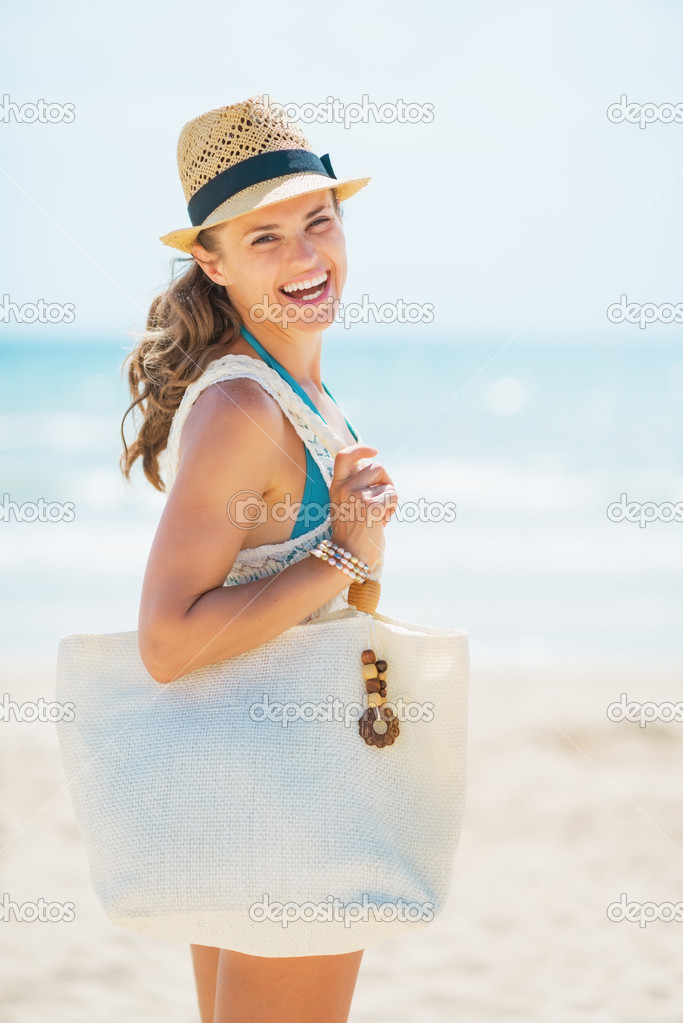 Portrait of happy young woman in hat and with bag on beach
