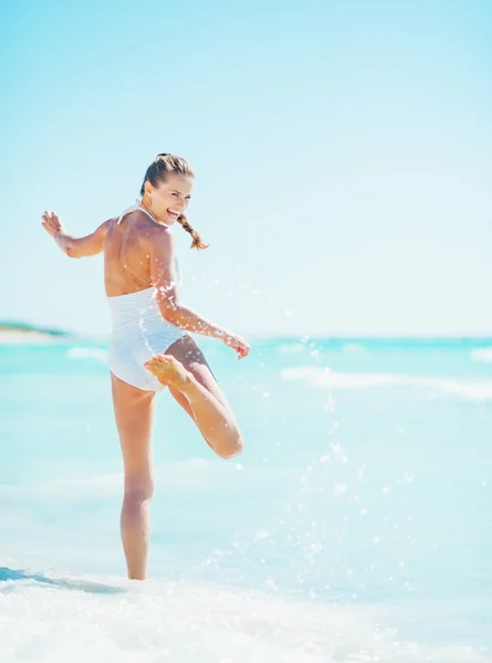 Ganzkörperporträt einer lächelnden jungen Frau, die am Strand mit Wellen spielt — Stockfoto