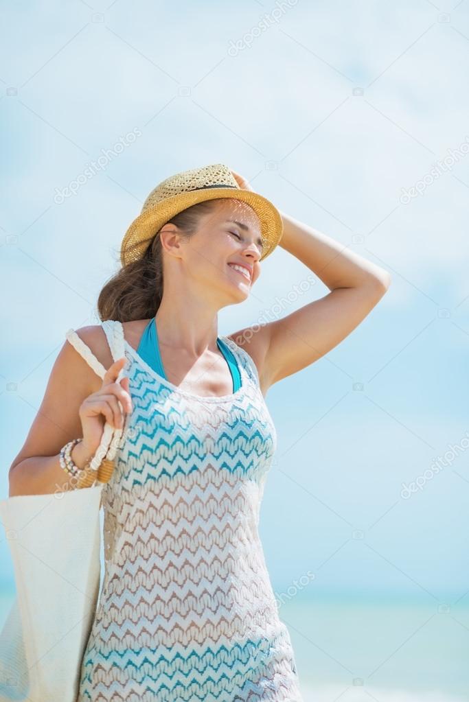 Portrait of happy young woman with hat and bag on sea shore