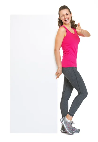 Full length portrait of fitness young woman showing blank billboard and thumbs up — Stock Photo, Image