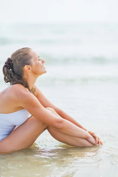 Mujer joven disfrutando sentado en la costa del mar — Foto de Stock