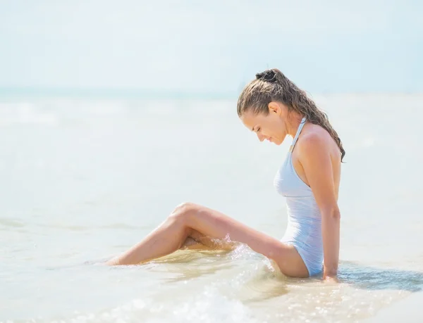 Mujer joven en traje de baño sentado en la costa del mar — Foto de Stock