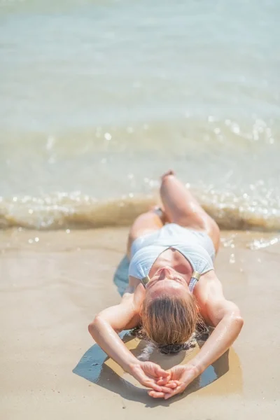 Primer plano de la mujer joven en traje de baño que pone en la orilla del mar — Foto de Stock