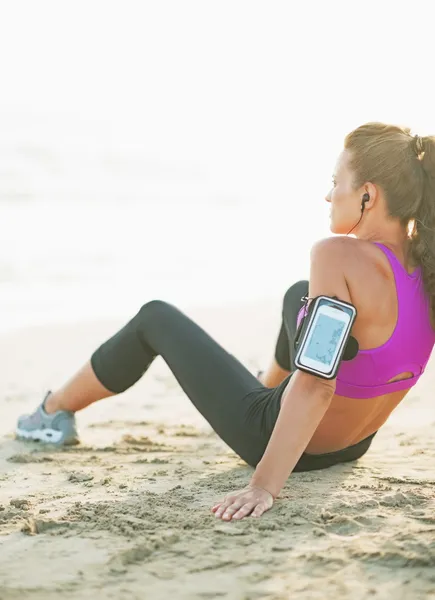 Mujer joven de fitness sentada en la playa. visión trasera —  Fotos de Stock