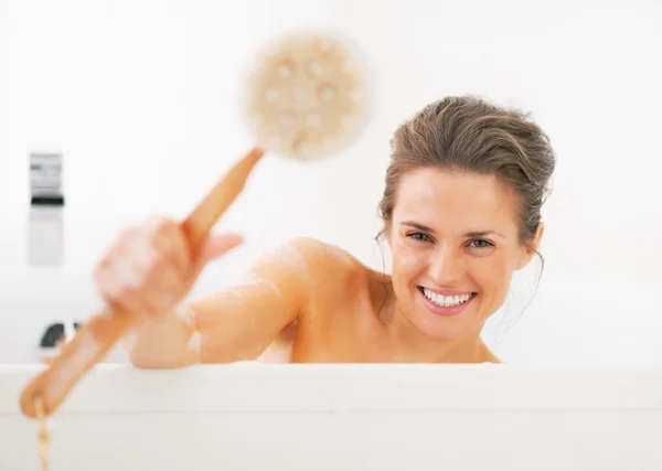 Улыбающаяся молодая женщина показывает кисть для тела в ванной — стоковое фото