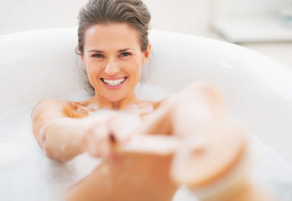 Sorridente giovane donna che si lava con la spazzola per il corpo nella vasca da bagno — Foto Stock