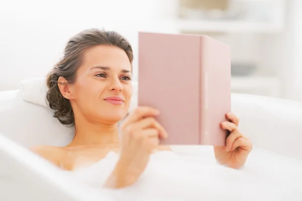 Happy young woman reading book in bathtub — Stock Photo, Image