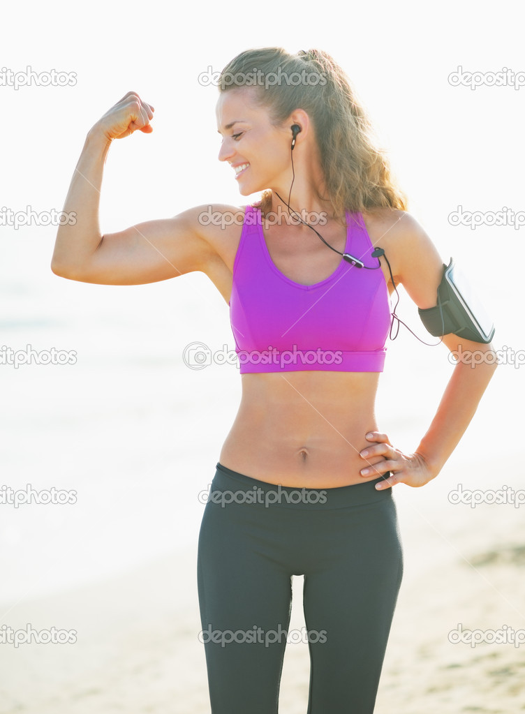 Smiling fitness young woman showing biceps