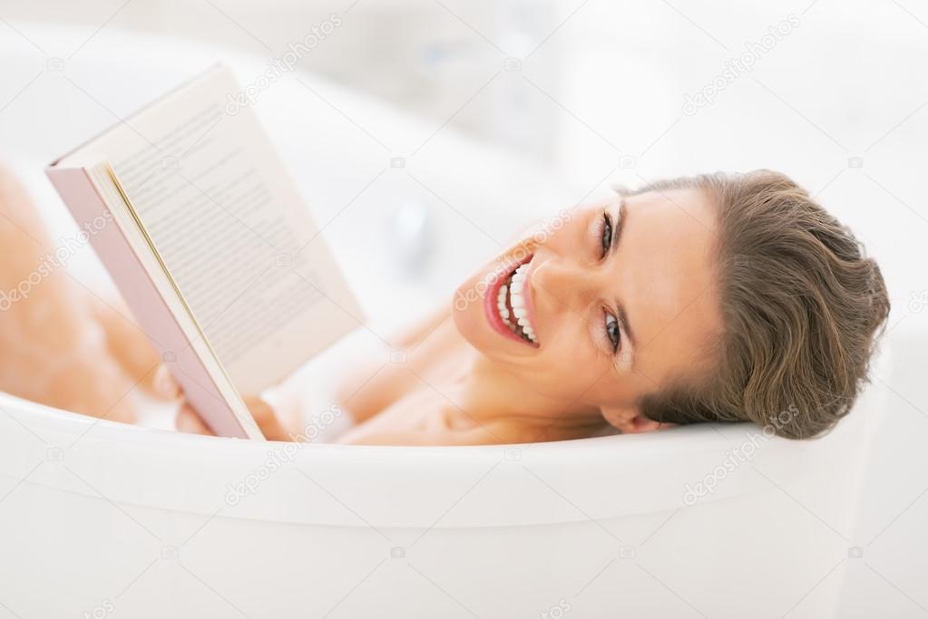 Portrait of smiling young woman reading book in bathtub