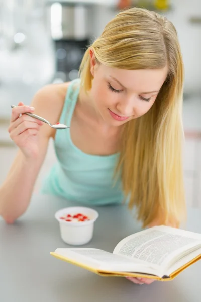 Mulher comendo iogurte e livro de leitura — Fotografia de Stock