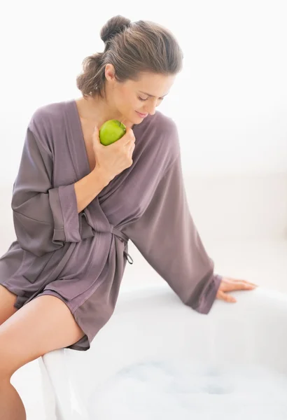 Avslappnad ung kvinna sitter på badkar med äpple — Stockfoto