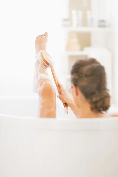 Mulher na banheira usando escova de corpo na perna — Fotografia de Stock