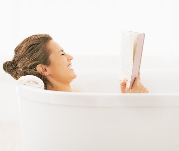 Smiling young woman in bathtub reading book