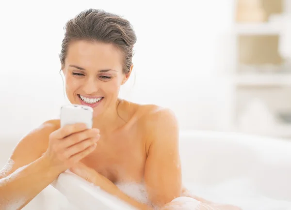 Young woman in bathtub writing sms — Stock Photo, Image