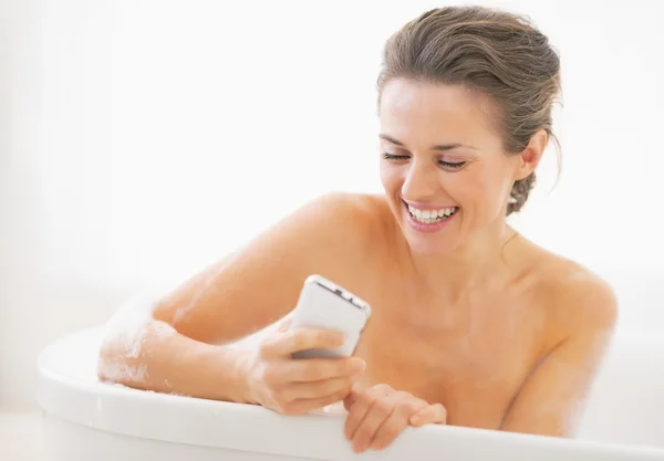 Sorridente giovane donna in vasca da bagno scrivere sms — Foto Stock
