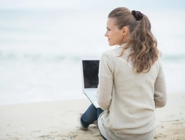 Woman sitting with laptop on cold beach — Stock Photo, Image