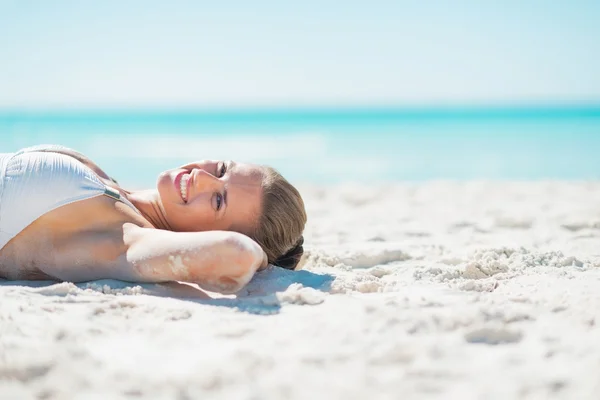 Lächelnde junge Frau bräunt sich am Strand — Stockfoto