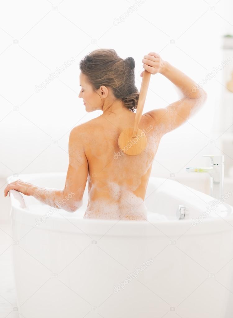 Woman using body brush in bathtub.