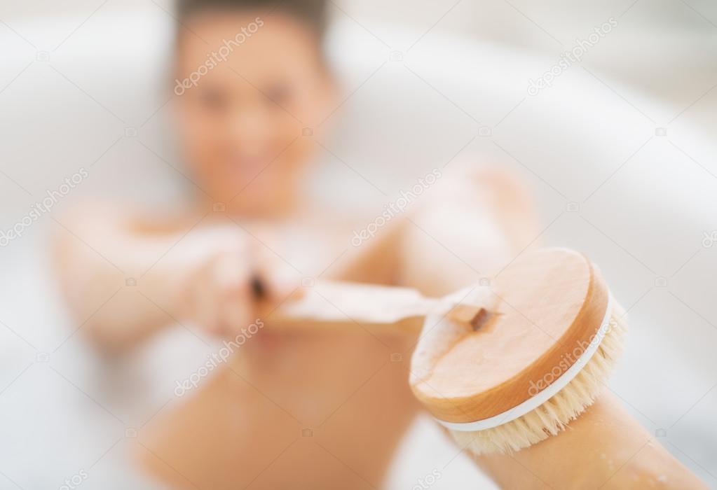 Woman in bathtub using body brush