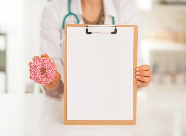 Médico mostrando área de transferência em branco e donut — Fotografia de Stock