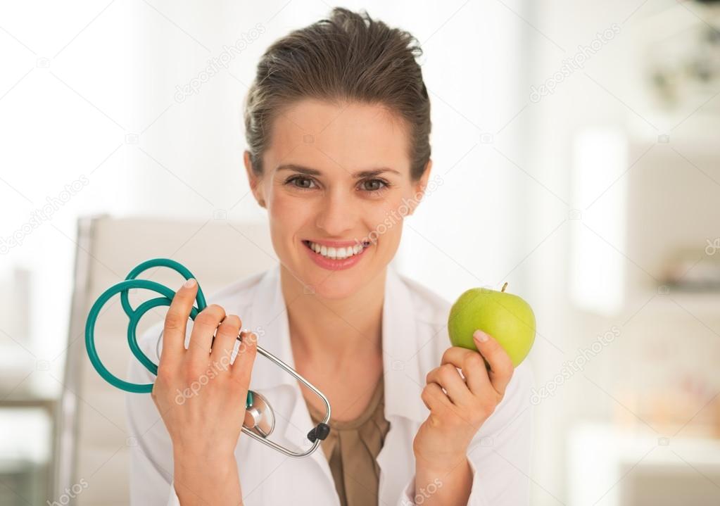 Happy medical doctor woman showing apple and stethoscope