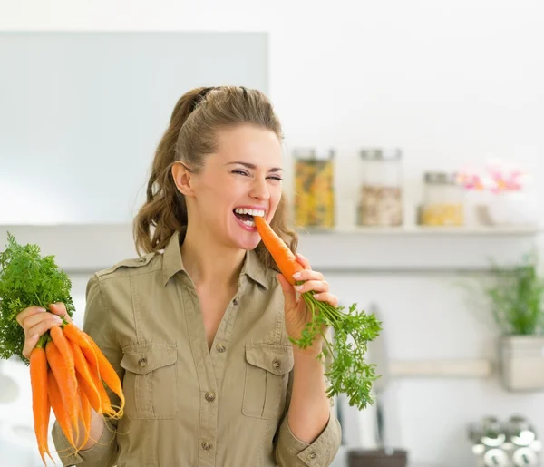 Femme au foyer manger de la carotte dans la cuisine — Photo