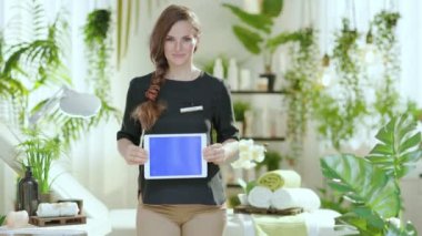 happy woman worker in modern beauty studio showing tablet PC blank screen.
