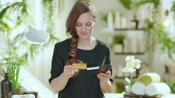 在现代美容院的电子商务网站上 40岁的女性员工带着智能手机和信用卡在线购物 面带微笑 — 图库视频影像