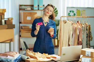 Ofiste akıllı telefon kullanan, kredi kartı olan, yorgun, küçük işletme sahibi bir kadın..