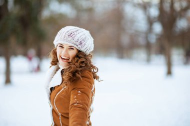 Şehir parkında kışın örgü şapka ve kuzu postuyla mutlu ve şık bir kadın..