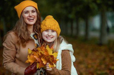 Hello autumn. happy young mother and daughter in orange hats with autumn yellow leaves outside on the city park in autumn.