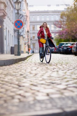 stylish woman in red rain coat outdoors in the city riding bicycle.